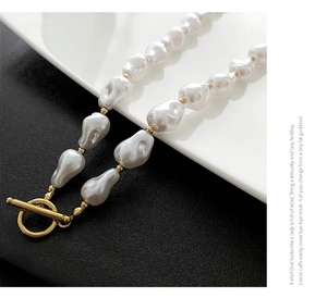 Detailed close-up of baroque pearl necklace with golden OT clasp on a white plate