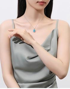 Detail showing an emerald-cut blue gemstone pendant on a silver necklace worn by a model