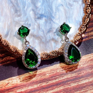 Close-up of teardrop emerald green zircon earrings with cubic zirconia halo in silver setting