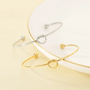 Minimalist stainless steel knot cuff bracelets in gold and silver finish shown on white plate