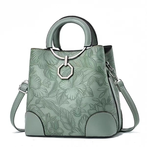 Dettaglio della borsa verde salvia con motivi floreali a rilievo e manico ad anello in metallo.