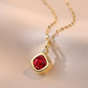 Macro shot of square red gemstone pendant on a gold chain over champagne silk fabric