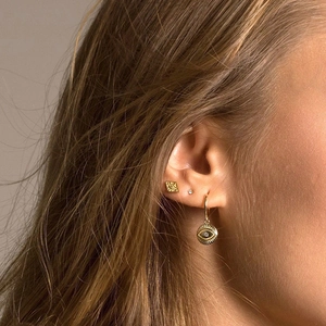 Detail view of gold Evil Eye hoop earrings and stud set worn on ear for women