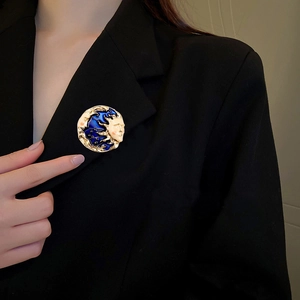 Detail of sun and moon face brooch with blue enamel on a black blazer jacket lapel