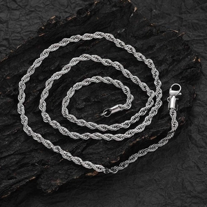 Detailed macro shot of a silver steel rope chain necklace on a dark textured rock base