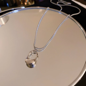 Minimalist silver stainless steel necklace with geometric pendant on a reflective surface