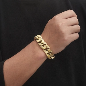 Close-up of men's chunky gold Cuban chain bracelet with engraved ancient patterns
