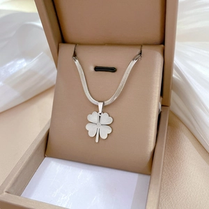 Detail of silver clover pendant on flat snake chain inside a beige jewelry gift box