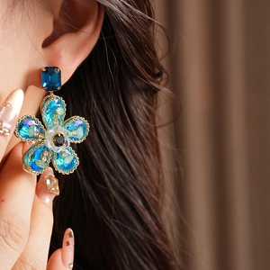 Gros plan de boucles d'oreilles fleurs en cristal bleu vintage dorées sur modèle