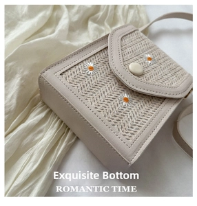 Detail showing straw woven texture and white daisy embroidery on the beige crossbody bag