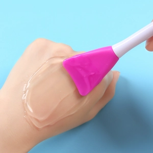 Pink dual-ended silicone mask brush applying smooth foundation on hand skin