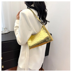 Detail of metallic gold crocodile pattern underarm bag worn by a model in lifestyle setting