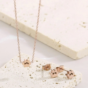 Detail view of rose gold paw print necklace and earrings set on a stone surface