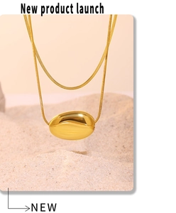 Macro shot of a minimalist gold bean pendant with a sleek snake chain on a sandy background