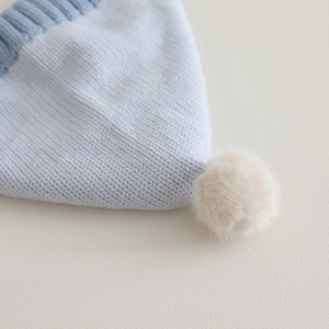 Light blue knit baby bonnet with a soft cream pom-pom and ribbed edge detailing