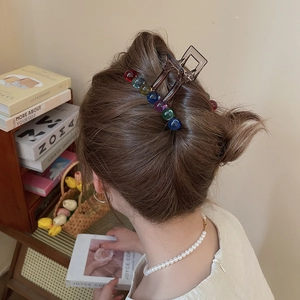 Detail of a large acrylic shark clip with rainbow beads on dark brown hair