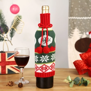 Knitted Christmas wine bottle cover with snowflake patterns and red pom-poms on table
