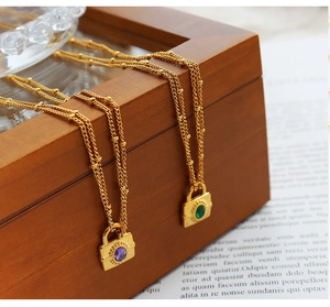 Detail of gold padlock pendants with purple and green stones on layered chains