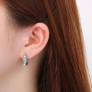 Detail view of silver textured C-shaped earrings with pearls worn on the ear lobe