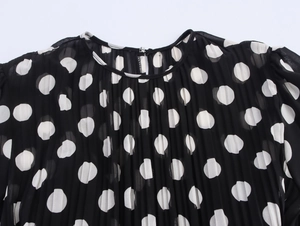 Detail of round neckline and white polka dots on pleated black chiffon fabric
