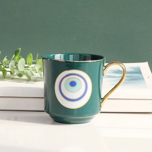 Detail of dark green ceramic evil eye mug with gold rim and circular handle on desk