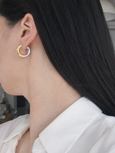 Close-up of dual-tone gold and silver metal hoop earrings worn by a model in a natural setting