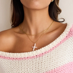 Détail d'un collier double chaîne dorée avec un pendentif croix en perles d'eau douce