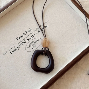 Close-up of wood resin geometric pendant with amber bead on a brown necklace cord