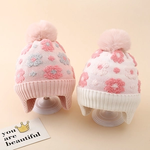 Close-up of winter floral knit hats with pink faux fur pom-poms and soft warm lining