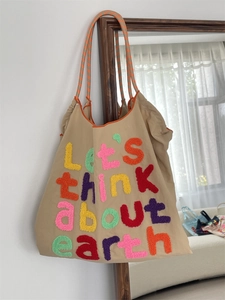 Close-up of khaki canvas tote with colorful 3D flocked Let's think about earth embroidery