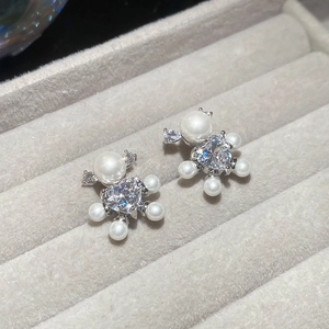 Detail of silver bear earrings with heart zircon and pearls on a grey jewelry tray