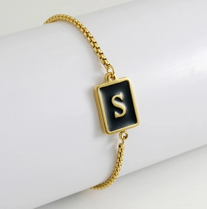 Close-up of gold stainless steel box chain bracelet featuring a black pendant with letter S