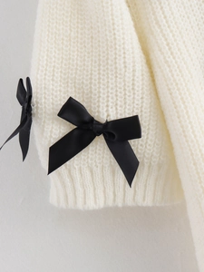 Gros plan détaillé des poignets d'un pull en maille blanc avec des nœuds en satin noir