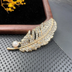 Detailed close-up of a golden feather brooch with pavé rhinestones and a pearl on velvet