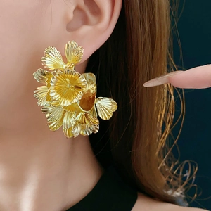 Close-up of a large metallic golden flower earring worn by a model in soft lighting