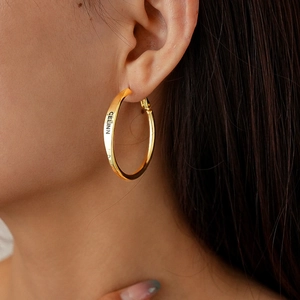Close-up of polished gold-finish circular hoop earrings featuring letter engraving