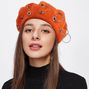 Detail of orange wool beret featuring decorative metal rings on a model