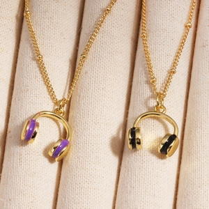 Detail of colorful enamel headphone pendants on golden necklaces on a beige display stand