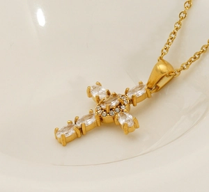 Macro shot of gold cross necklace with shimmering zircon stones resting in a ceramic bowl