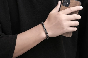 Detail of vintage braided titanium steel bracelet on male wrist holding a wooden phone