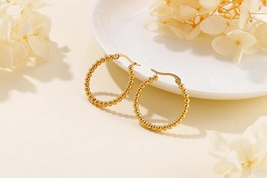Detailed view of gold beaded hoop earrings featuring a textured sphere design on a warm background