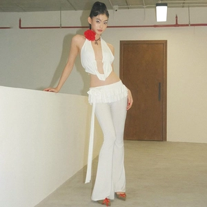 Dettaglio del top bianco con scollo a V, fiore rosso e pantaloni a zampa con volant