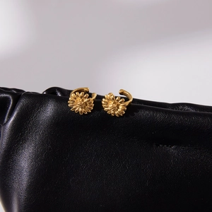 Detail of golden daisy clip-on earrings displayed on a black leather texture backdrop