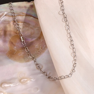 Macro detail of silver heart-shaped chain links on elegant pearl and silk background