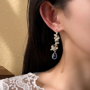 Close-up of golden butterfly earrings with blue water-drop gems on a female model