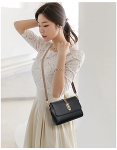 Close-up of elegant black leather crossbody bag with brown strap and gold metal buckle
