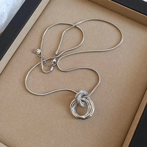 Detail view of silver multi-layered circular pendant on a snake chain over a jewelry tray