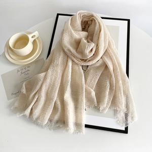 Detail of beige pleated cotton linen scarf with frayed edges styled on a white table