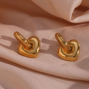Detailed close-up of golden heart pendants on polished earrings over pink silk fabric