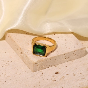 Close-up of a gold rectangle green gemstone ring on a stone base with cream silk fabric